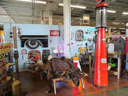 A vintage-themed display featuring old signs, a red gas pump, and rustic furniture in a spacious indoor market.