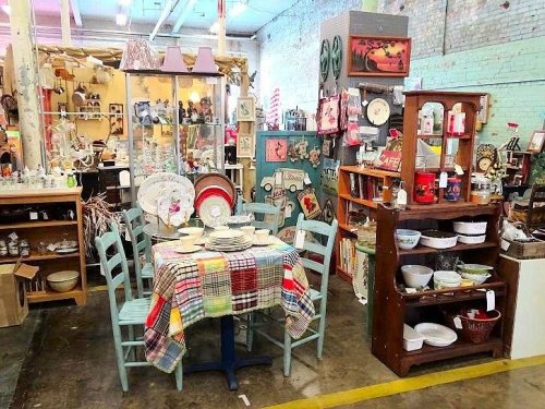 A vintage shop display featuring a table with plates, colorful chairs, and various antiques on shelves.