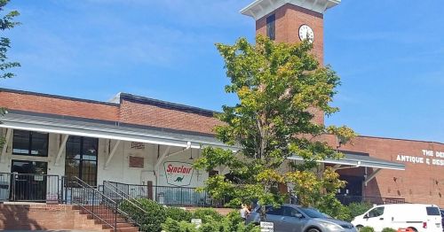 A brick building with a clock tower, featuring a Sinclair sign and a tree in front, under a clear blue sky.