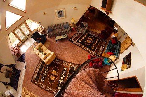 A spacious, circular living room with colorful rugs, sofas, and a spiral staircase, viewed from above.