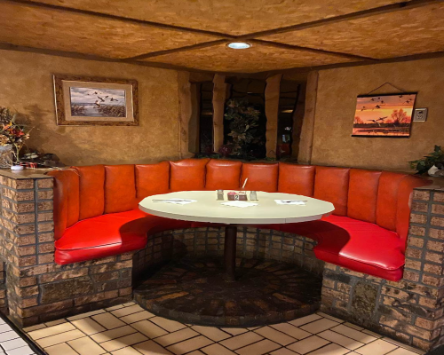 Cozy restaurant booth with orange seating and a round table, set against a textured wall and decorated with artwork.