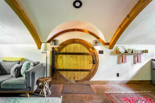 Cozy interior featuring a wooden door, arched ceiling, sofa, and decorative shelves with dishware.