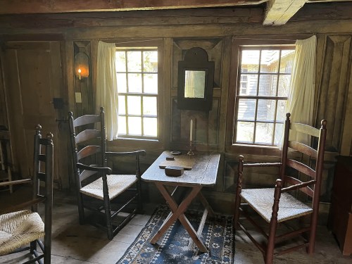 Cozy interior of a rustic room with two windows, a wooden table, and two chairs, illuminated by natural light.