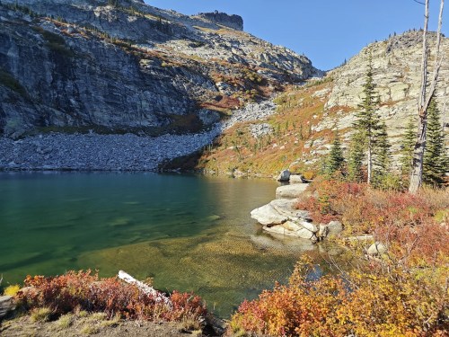 A serene lake surrounded by rocky cliffs and colorful autumn foliage under a clear blue sky.