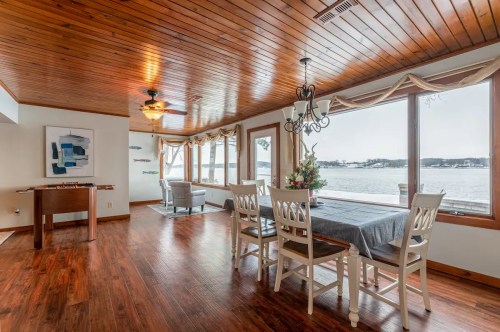 Bright dining area with wooden ceiling, a table set for four, and large windows overlooking a scenic waterfront view.