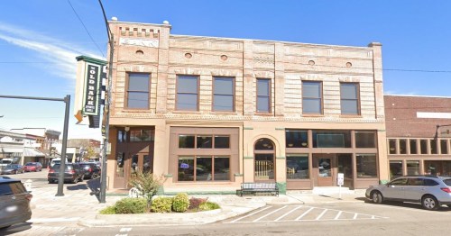 Historic brick building with large windows and decorative details, located on a street corner in a town.