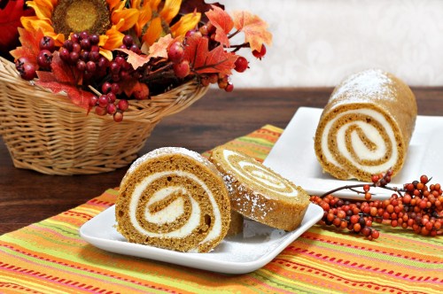 Fluffy pumpkin roll with layers of cream cheese icing on a table with beautiful fall decor.