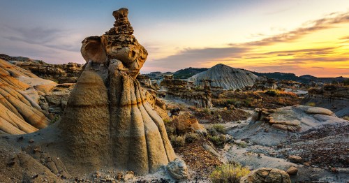 A stunning landscape featuring unique rock formations at sunset, with layered hills and a colorful sky.