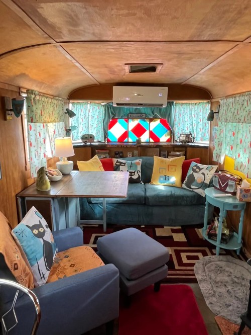 Cozy interior of a vintage trailer, featuring colorful cushions, a table, and decorative curtains with a warm ambiance.