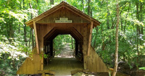 A wooden covered bridge surrounded by lush green trees, leading to a peaceful forest path.