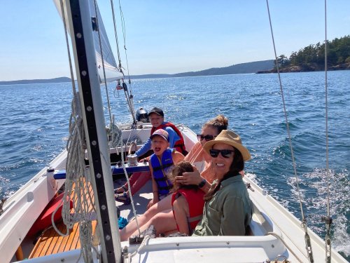 A family enjoys a sunny day sailing on a boat, smiling and relaxing on the water with scenic views in the background.