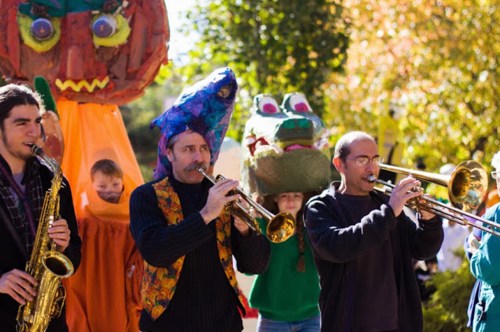 A lively parade with musicians playing instruments, colorful costumes, and large puppets in a festive outdoor setting.