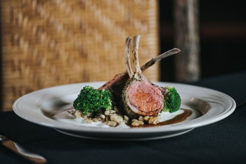 A plate of lamb chops with broccoli and a creamy sauce, elegantly presented on a black tablecloth.