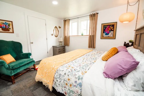 Cozy bedroom featuring a bed with colorful bedding, a green armchair, and natural light from a window.