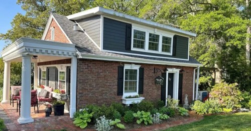 A charming two-story house with a brick exterior, white trim, and a landscaped garden in front.