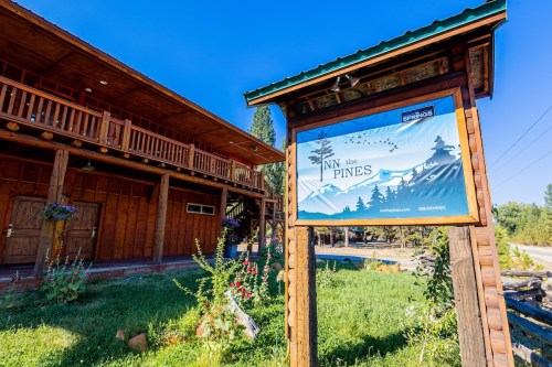 Sign for "Inn the Pines" in front of a rustic wooden building surrounded by greenery and mountains.