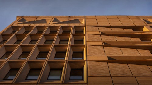 A modern building facade with geometric patterns and textured surfaces, illuminated by warm sunlight.