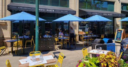 Outdoor dining area at Huli Sue's with blue umbrellas, yellow chairs, and tables set for guests.
