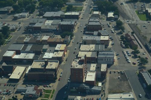 Aerial view of a city block featuring various buildings, streets, and parked cars under a clear sky.