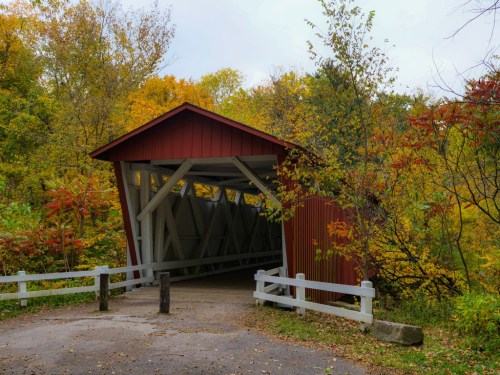 The red-painted wooden Everett Covered Bridge in Cuyahoga Valley National Park, Peninsula, Ohio, surrounded by orange, green, and red fall foliage.