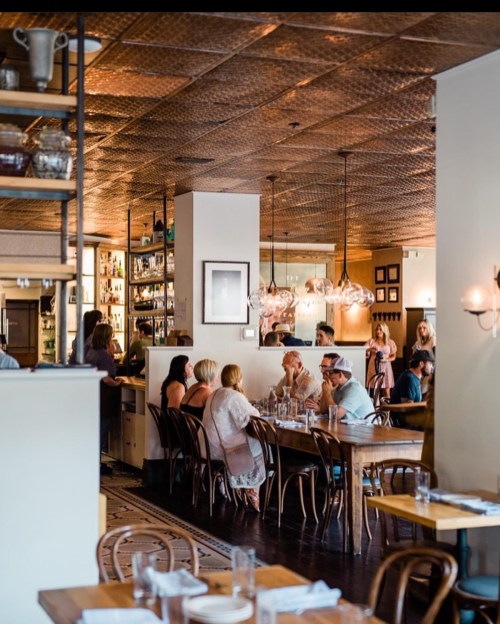 A bustling restaurant interior with wooden tables, patrons dining, and a stylish copper ceiling.