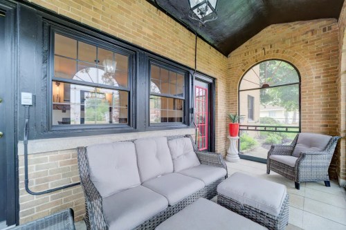Cozy porch with wicker furniture, large windows, and a potted plant, featuring brick walls and a welcoming atmosphere.
