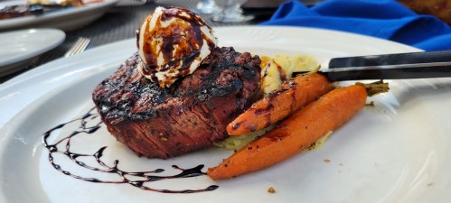 A perfectly cooked steak topped with a dollop of sauce, served with roasted carrots and a drizzle of balsamic reduction.