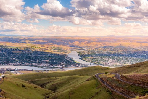 A panoramic view of rolling hills and a river winding through a valley under a partly cloudy sky.