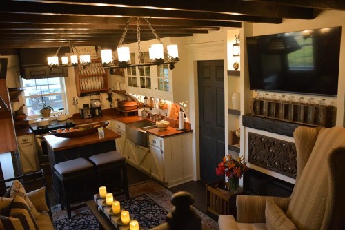 Cozy living space with a kitchen area, wooden beams, a TV, and candles on a coffee table, creating a warm atmosphere.