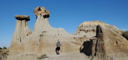 A person stands near unique rock formations under a clear blue sky, showcasing natural erosion and geological features.