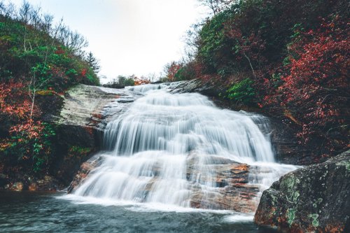 A serene waterfall cascading over rocks, surrounded by lush greenery and autumn-colored foliage.