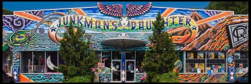 Colorful mural on a store facade featuring a UFO, mountains, and vibrant designs, titled "Junkman's Daughter."