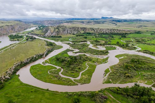 Aerial view of winding rivers through lush green landscapes and rolling hills under a cloudy sky.