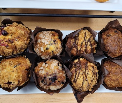 A variety of muffins in brown paper liners, featuring flavors like blueberry, chocolate, and streusel topping.