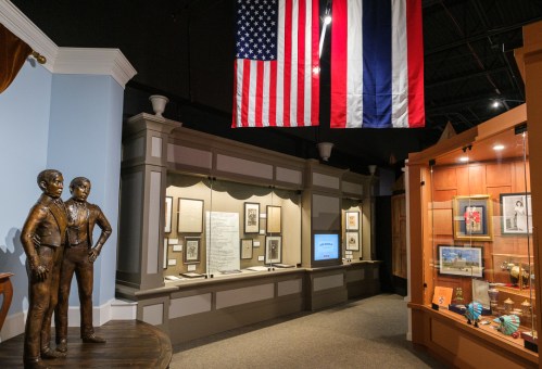 Museum interior featuring a statue of two men, display cases, and flags hanging from the ceiling.