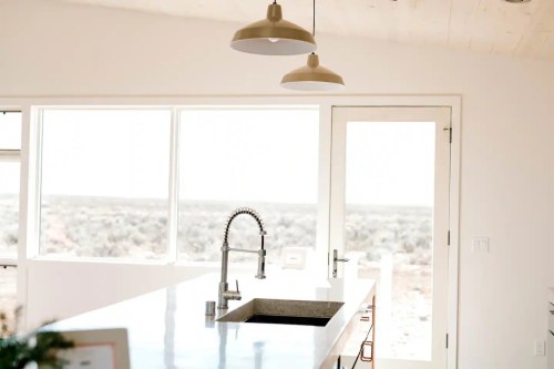 Modern kitchen with a sleek countertop, sink, and large windows overlooking a desert landscape.