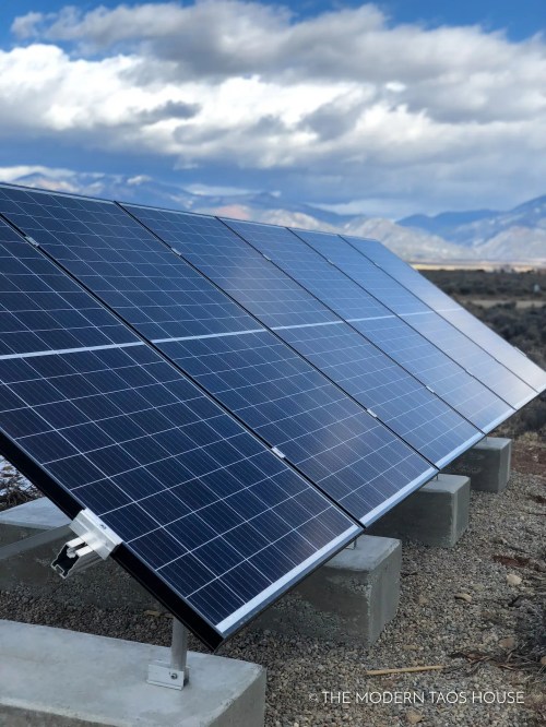 Solar panels installed on concrete mounts, set against a backdrop of mountains and cloudy skies.