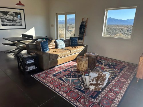 Cozy living space with a brown sofa, patterned rug, and large window showcasing a mountain view.
