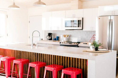 Modern kitchen with white cabinets, stainless steel appliances, and red bar stools at a concrete island.