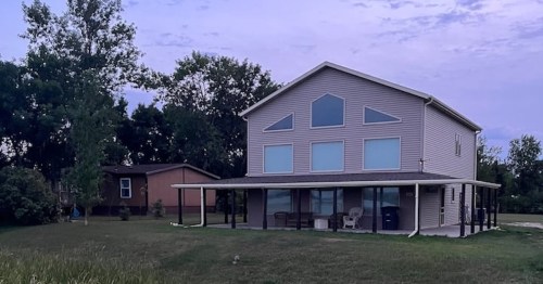 a charming rural house with a large field of grass in the front and a purple sky above