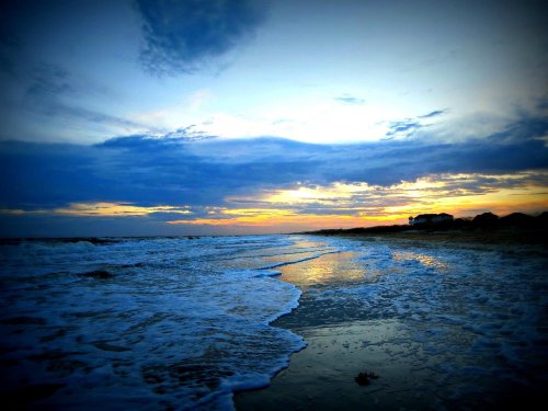 A serene beach at sunset, with gentle waves lapping at the shore and a colorful sky filled with clouds.