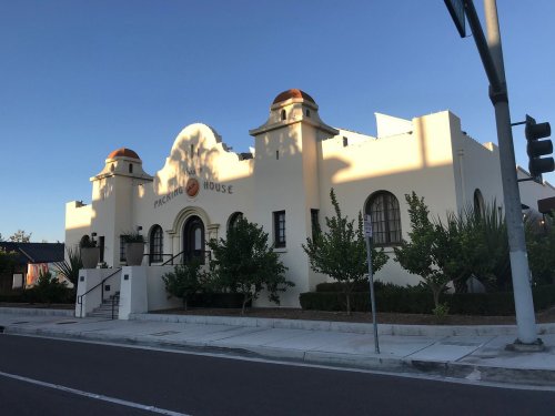 A white building with a red-tiled roof and decorative features, surrounded by greenery, under a clear blue sky.