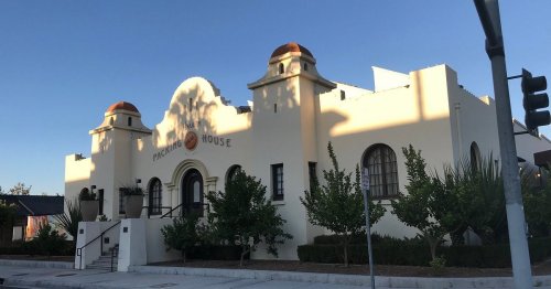 A white building with a decorative facade and two domed towers, surrounded by greenery and clear blue skies.