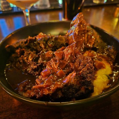 A close-up of a bowl filled with tender, dark-braised meat in rich sauce, served over creamy mashed potatoes.