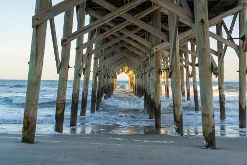 The view underneath an old rustic wooden fishing pier at sunset. Pawleys Island, South Carolina.