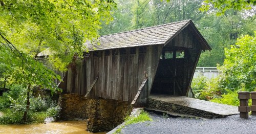 A rustic wooden covered bridge surrounded by lush green trees under a clear blue sky.