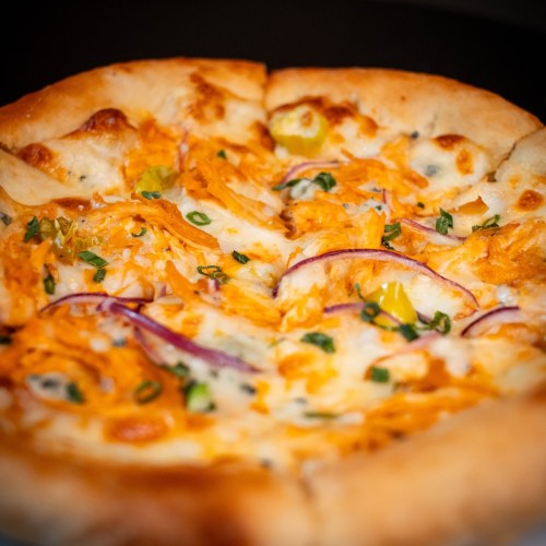 A close-up of a pizza topped with cheese, shredded orange vegetables, red onion, and green herbs on a golden crust.
