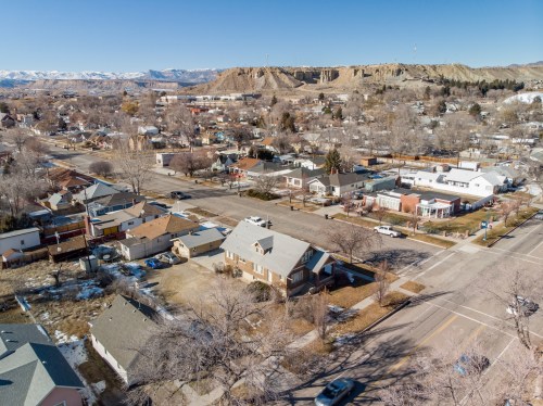 Aerial view of a small town with residential homes, streets, and distant mountains under a clear blue sky.