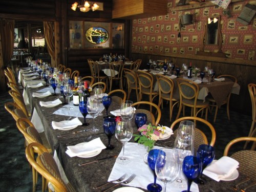 A beautifully set dining room with elegant tables, blue glassware, and floral centerpieces in a cozy atmosphere.