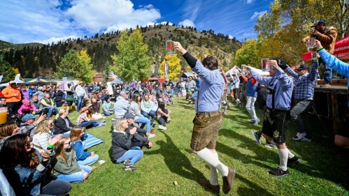 A lively outdoor festival scene with participants in traditional attire raising drinks, while a crowd watches and enjoys.